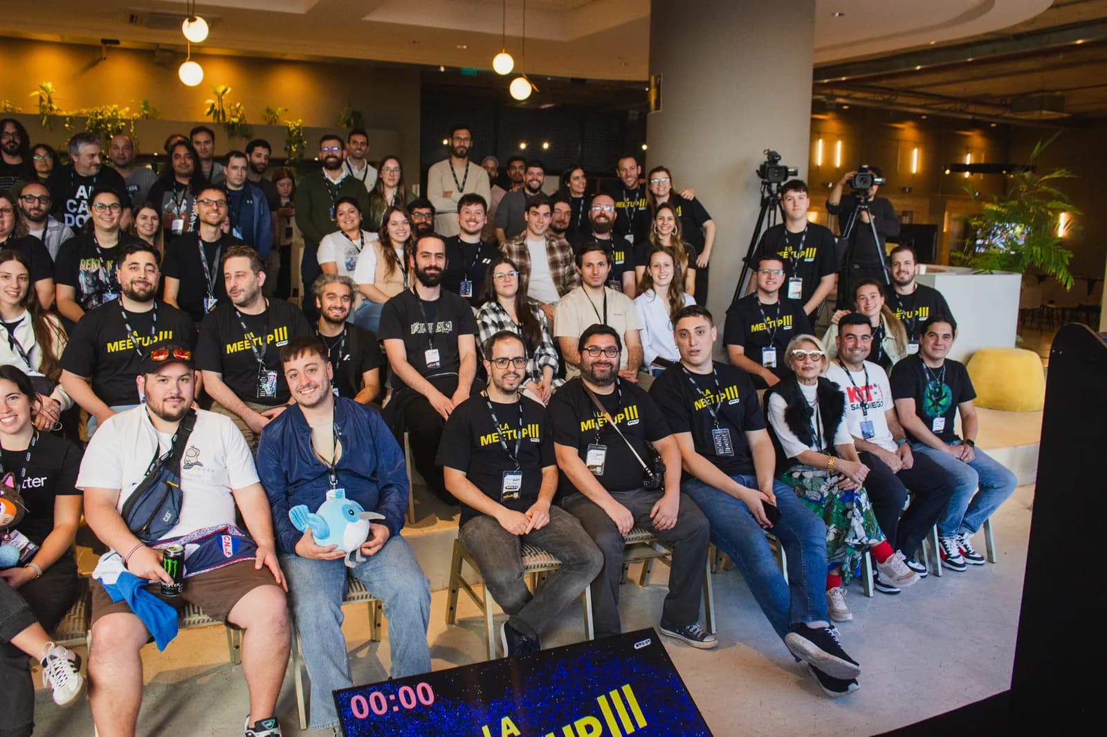 Toda la sala de La Meetup III con los brazos en alto para la foto grupal